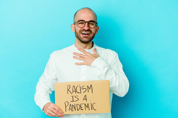 Young caucasian bald man holding a racism is a pandemic isolated on white background laughs out...