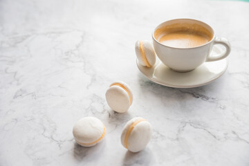 Coffee and French macaroons on marble background.Cup of aromatic coffee cappuccino with white cookies and sprinkled grains of natural roasted coffee