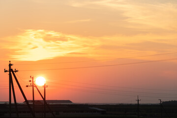 pink sunset over the poles of power lines. A large sun on the horizon line between the wires.