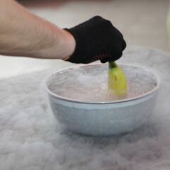 Men  hand in black glove takes out a banana from a bowl of liquid nitrogen on the table close up,...