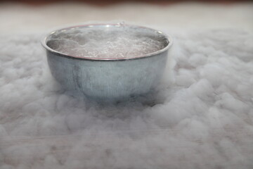 Liquid nitrogen in stainless steel bowl on table with transpiration mist smoke close up side view