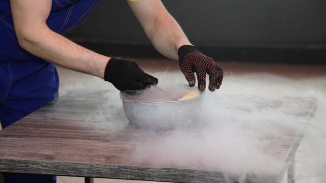 Male magician's hands in black gloves place a banana in a bowl of liquid nitrogen on the table close up, fast cooling of the food