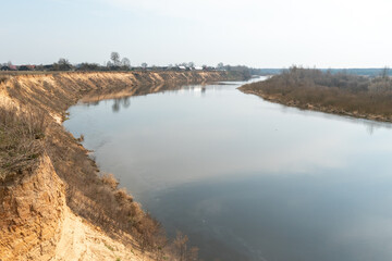 Fototapeta premium steep high river bank. A wide riverbed or channel. Yellow sand on the shore of an artificial pond.