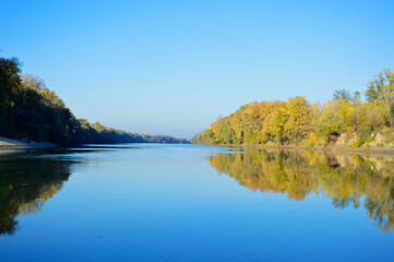 a river valley with gentle blue water and an autumn yellowing forest on the banks