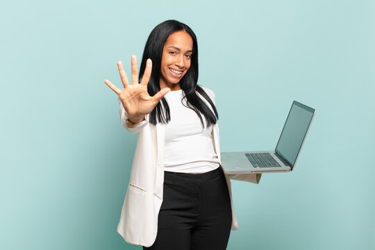 young black woman smiling and looking friendly, showing number five or fifth with hand forward, counting down. laptop concept
