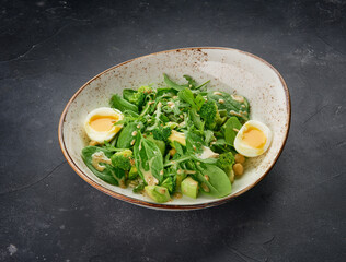 Tasty green healthy salad with spinach leaves, avocado and boiled eggs in bowl on dark slate background
