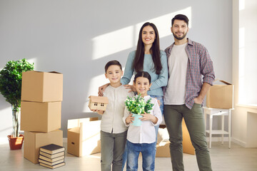 Relocating, new apartment for family concept. Young happy family with children son and daughter standing together in new flat and feeling cheerful with unpacking belongings