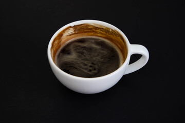 White cup of aromatic freshly ground arabica coffee on a black background. The cup is on the saucer. White cup of aromatic freshly ground arabica coffee on a black background. Top view.