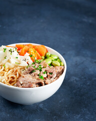 Poke bowl, pulled pork, vegetables, pumkin, soy beans edamame, noodles, on bowl, chopsticks. Copy space, closeup. Trendy asian food. Healthy, clean eating concept. Hawaiian dish, blue dark background.