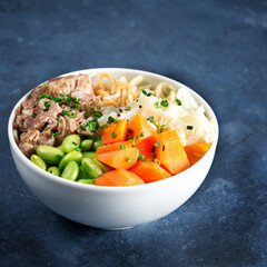 Poke bowl, pulled pork, vegetables, pumkin, soy beans edamame, noodles, on bowl, chopsticks. Copy space, closeup. Hawaiian dish, blue dark background. Trendy asian food. Healthy, clean eating concept.