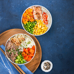 Two assorted poke bowls, flamed salmon, pulled pork, vegetables, rice, sauces. Top view, close-up. Hawaiian dish, blue dark background. Trendy asian food. Healthy and clean eating concept.