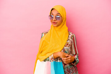Young muslim woman shopping some clothes isolated on pink background dreaming of achieving goals and purposes