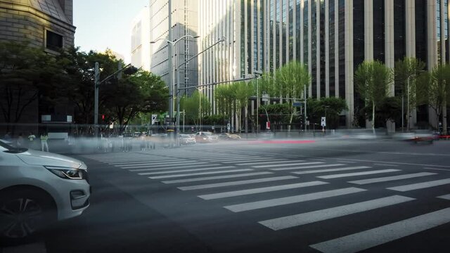 Timelapse of a busy crossroad in a big city in the evening. Cars stop at the traffic light and then move forward creating beautiful light trails.  Crowds of pedestrians cross the road in their turn.