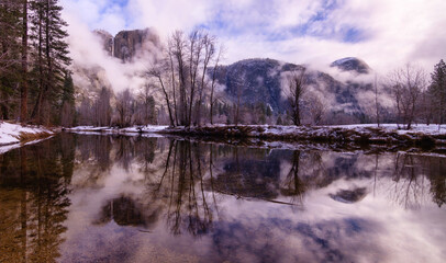 Panorama of Yosemite falls surrounded by low lying clouds reflected in the Merced river. 