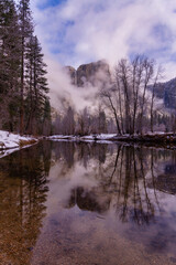 Yosemite falls framed by low lying clouds, reflected in the Merced river