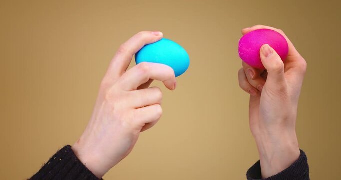 Easter Egg fight. Two hands with painted colourful eggs knock each other on beige studio background, close up video