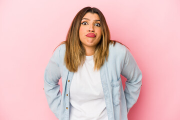 Young indian woman isolated on pink background shrugs shoulders and open eyes confused.