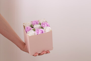 Female hand holding beautiful bouquet in pink box. White and purple roses in mock up box