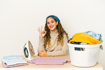 Young caucasian woman ironing clothes isolated cheerful and confident showing ok gesture.