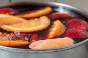 Red wine mulled wine with apples and oranges in the process of making at home in a stainless steel saucepan.