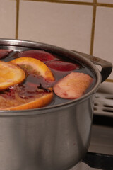 Red wine mulled wine with apples and oranges in the process of making at home in a stainless steel saucepan.