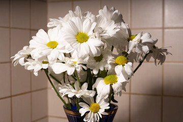 A bouquet of white daisies are in a blue vase. Some flowers have withered.