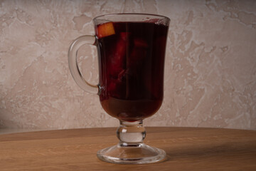 A glass of red wine mulled wine with apples and oranges is on a wooden table.