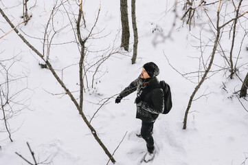 Fototapeta na wymiar A wanderer, a tourist in black clothes and a large backpack, walks through the snowy forest in winter. Photography, concept.