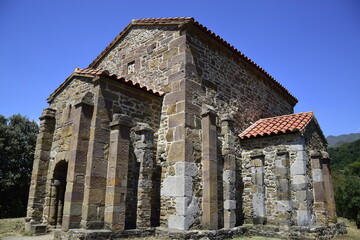 Fototapeta na wymiar Vista lateral de una iglesia católica perteneciente al estilo prerrománico asturiano, con mil doscientos años de antiguedad y situada en medio de las montañas cubiertas de bosques del norte de España