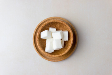 Sugar cubes in a wooden plates in center of the kitchen table. Top view