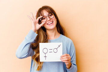 Naklejka premium Young caucasian woman holding a equality gender placard isolated excited keeping ok gesture on eye.