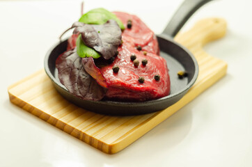 Raw beef fillet steak with spices on a small pan prepared for frying