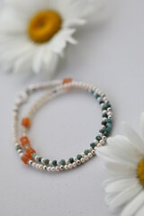 Bracelet of natural stones . Gemstone jewelry . Carnelian , crysocolla , pearls and citrine . Handmade jewerly on a white background with chamomiles.