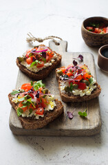 Open face sandwiches with soft cheese, tomatoes, capers and red onions on wooden cutting board close up