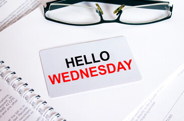 Text Hello Wednesday on a business card lying on a notepad with eyeglasses and text documents