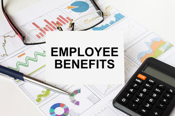 White card with text EMPLOYEE BENEFITS it is lies on financial charts with a calculator and eyeglasses