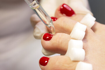 Pedicure nail coating with red gel polish and moisturizing cuticle oil in a beauty salon by a master. Close-up. Space for text