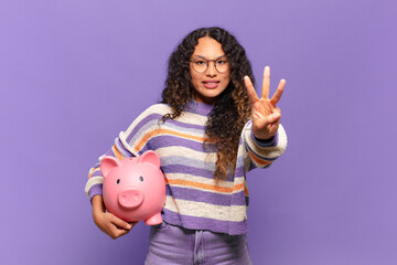 young hispanic woman smiling and looking friendly, showing number three or third with hand forward,...