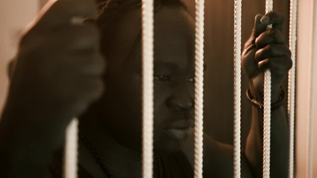 Depresed african american black man holding bars in the prison and shaking head. High quality 4k footage