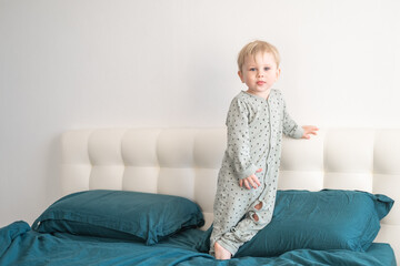 Little healthy blonde toddler boy in green pajamas having fun in bed at home