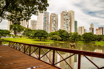 Fototapeta premium Lago no Parque Flamboyant, com prédios e céu com nuvens ao fundo em dias de lockdown.
