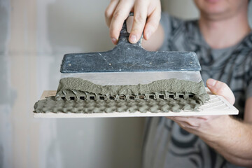 Comb trowel with cement mortar for gluing tiles. Tiling and home renovation. Waves from the glue on the tiles.