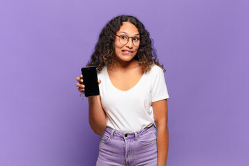 young hispanic woman looking puzzled and confused, biting lip with a nervous gesture, not knowing...