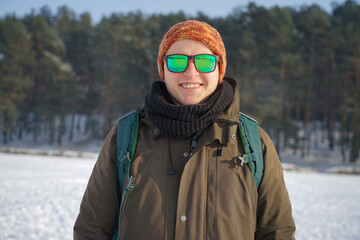 Fototapeta na wymiar A traveler in a hat and glasses in winter. Portrait of a guy in winter on the background of the forest and snow