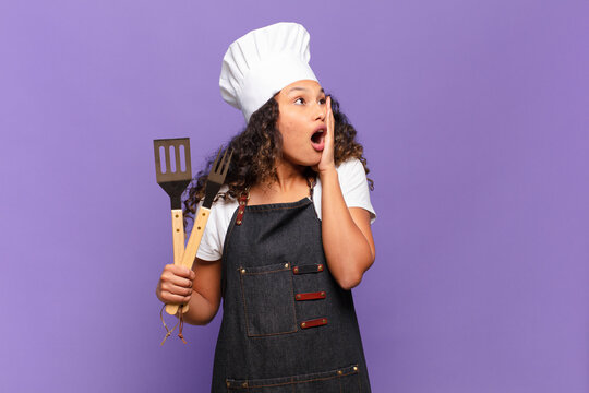 Young Hispanic Woman Feeling Happy, Excited And Surprised, Looking To The Side With Both Hands On Face. Barbecue Chef Concept