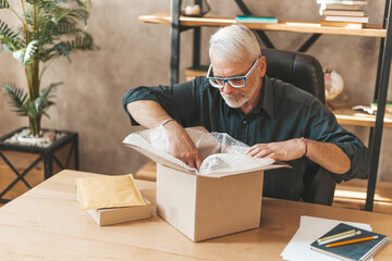 Online shopping package. A mature man opens the packaging at home. Fast delivery of mail to the...