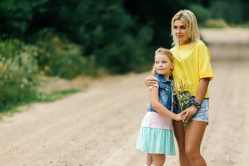 A young mother with her daughter, stand on the road in the forest and hug each other. Look away