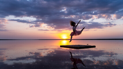 Silhouette of a gentle curly girl at sunset in the reflection of the golden sun. gymnast jump split in the air. The concept of freedom, ease