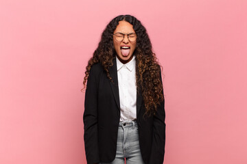 young hispanic woman with cheerful, carefree, rebellious attitude, joking and sticking tongue out,...