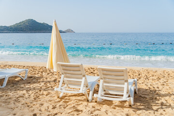 Two white plastic beach chairs on the beautiful beach near sea at sunny summer day.